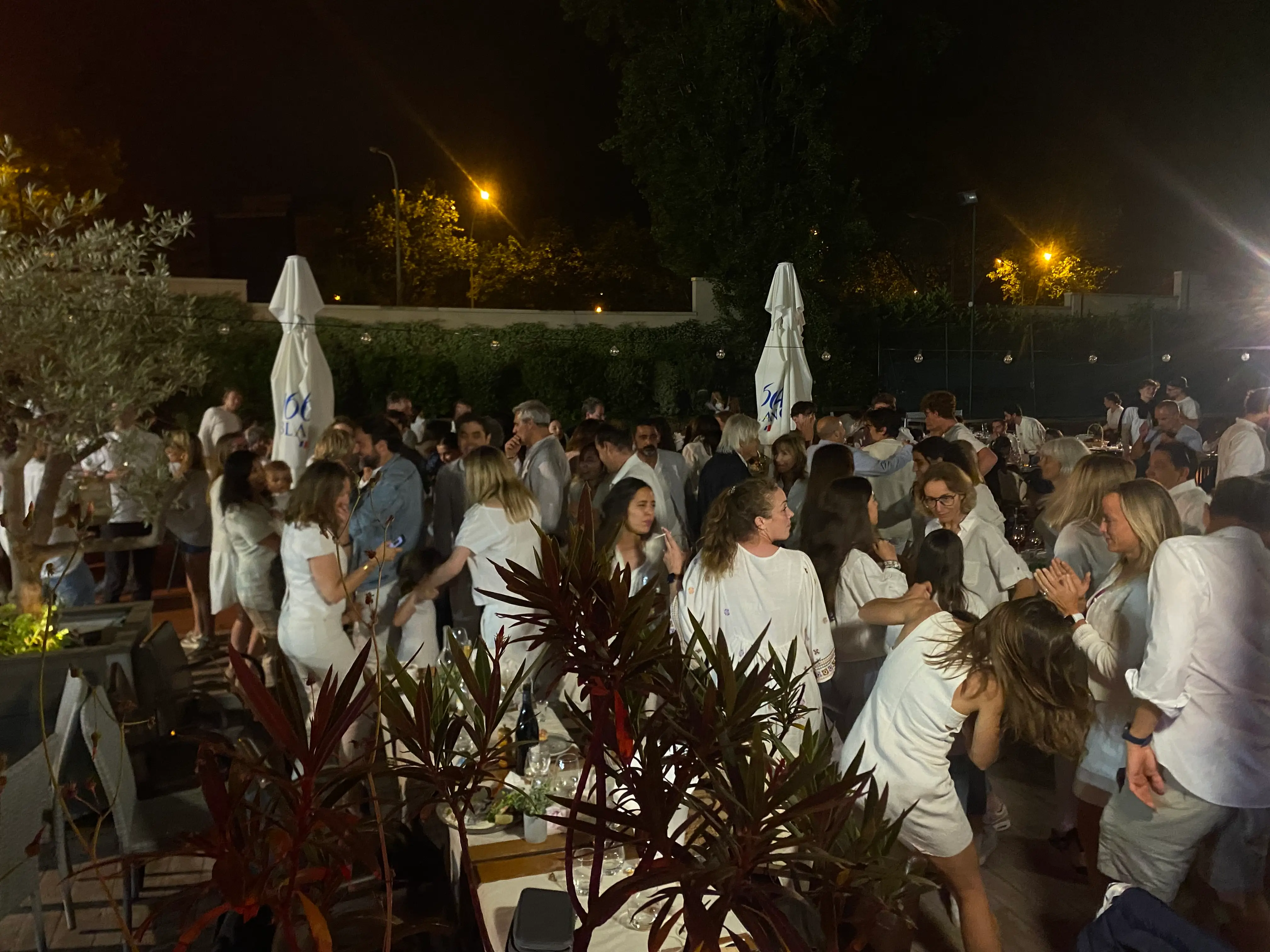 Invités habillés en blanc qui dansent en plein air, de nuit, pendant une soirée au tennis club du 16e arrondissement de Paris