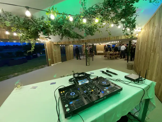 Contrôleur DJ et micros installés dans une salle de l'Hippodrome de Longchamp décorée de feuillage et de guirlandes lumineuses