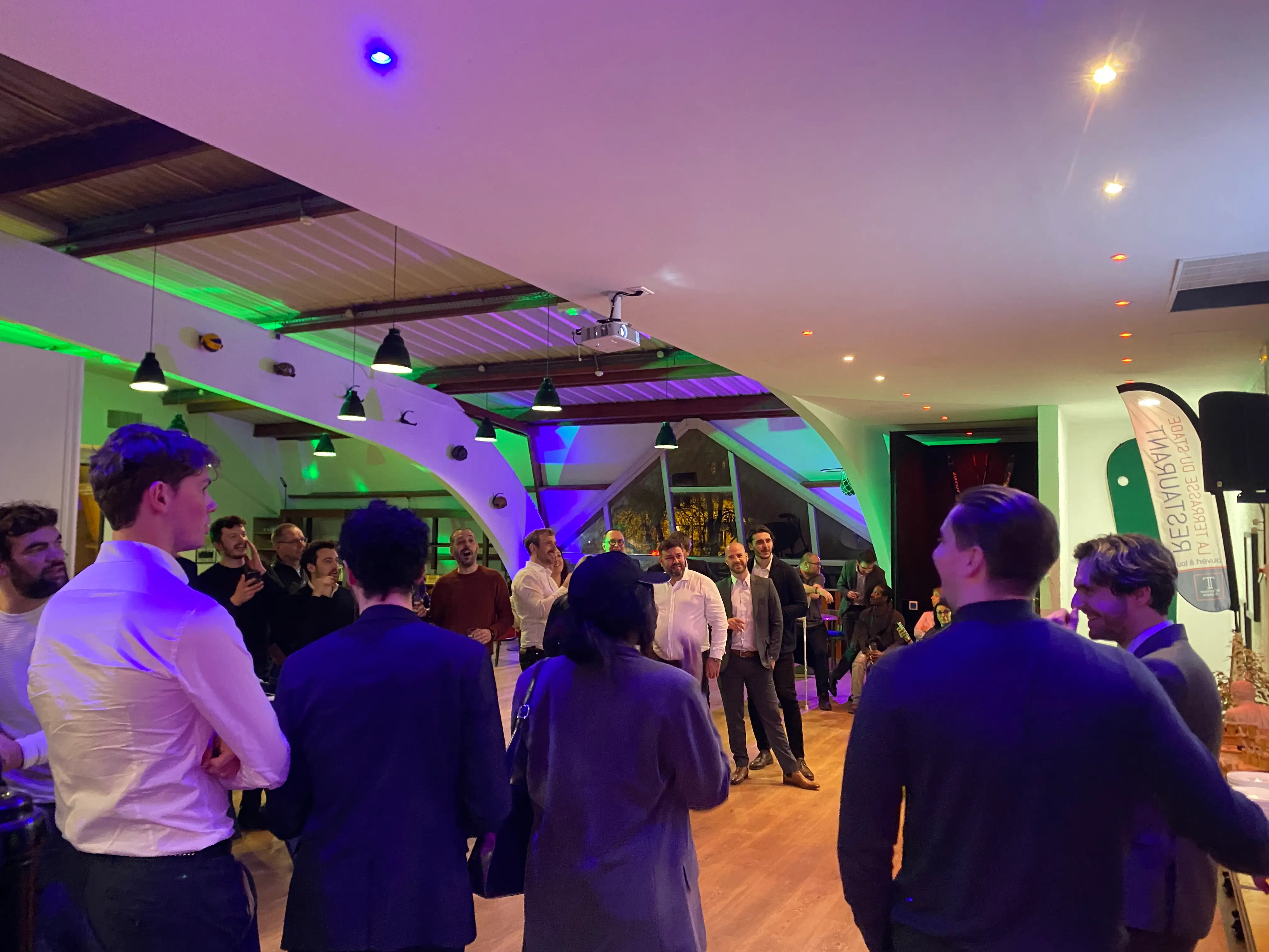 Collaborateurs réunis sous des lumières violettes et vertes pendant une soirée annuelle d'entreprise au restaurant La Terrasse du Stade