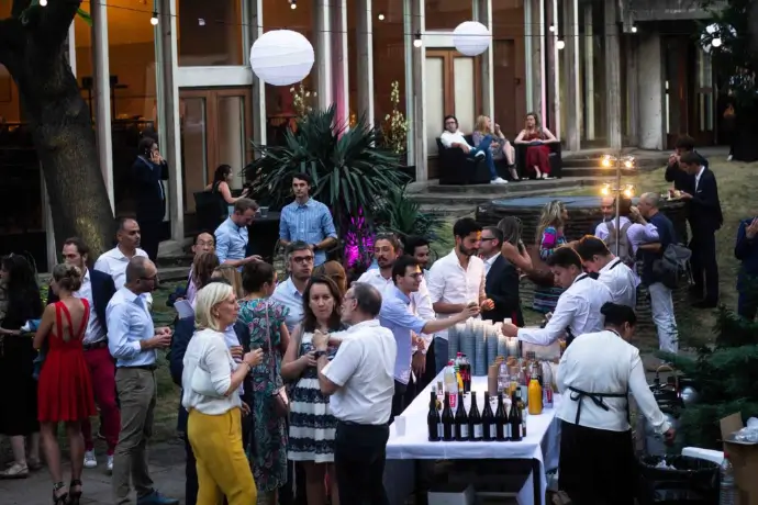 Invités autour d'un bar en plein air pendant une soirée d'entreprise, dans une cour arborée éclairée de lampions