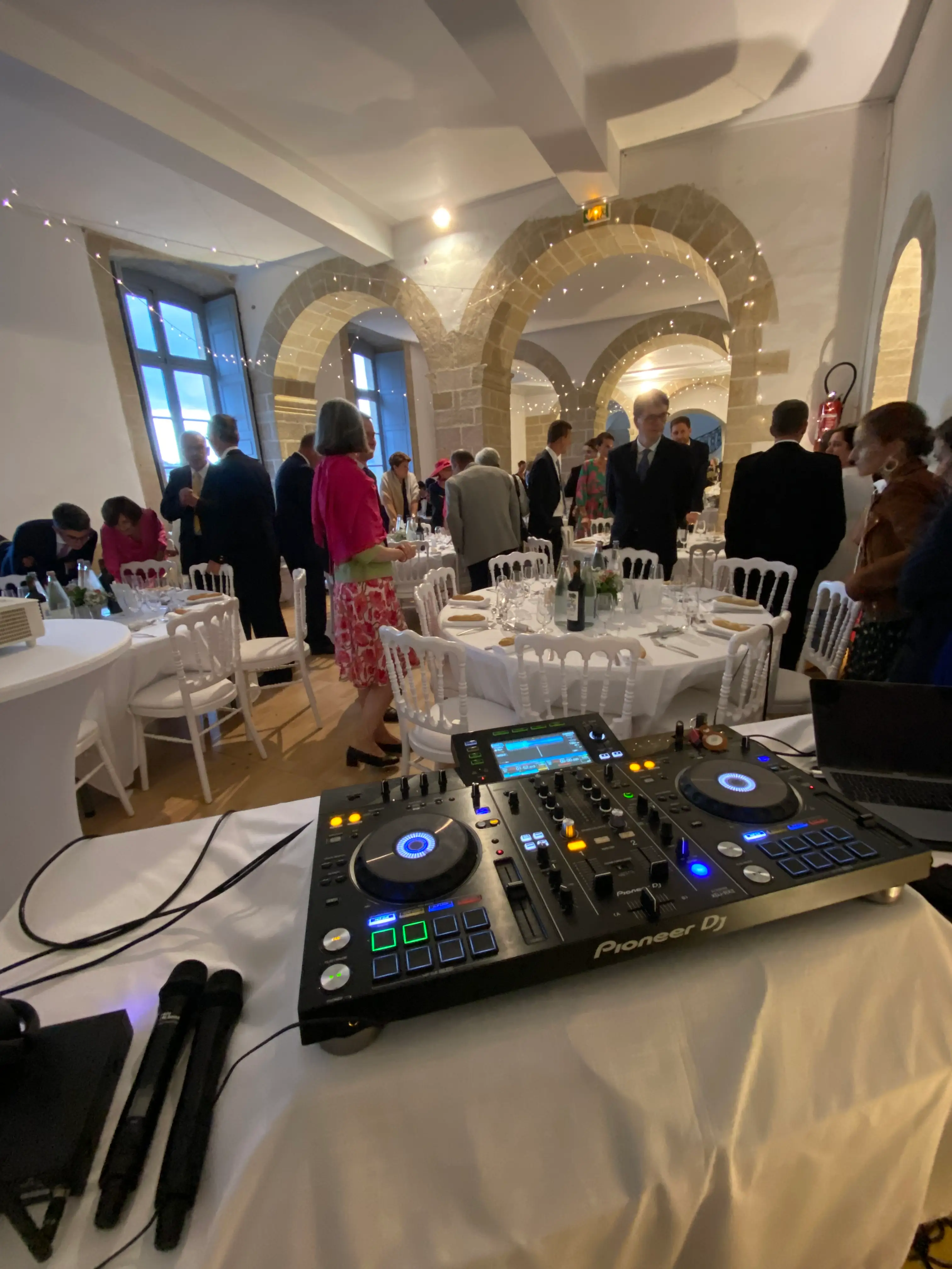 Contrôleur DJ et micros installés au bord d'une salle de réception de mariage dressée de tables rondes